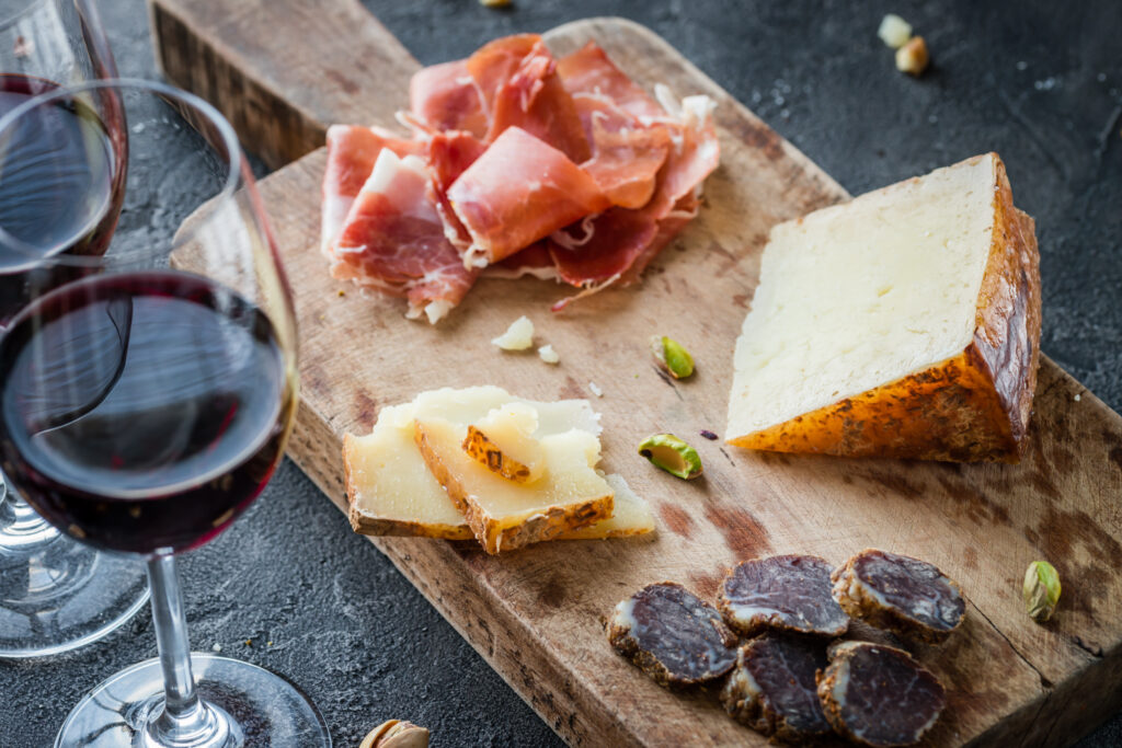 A wooden cutting board with cheese and meat on it.